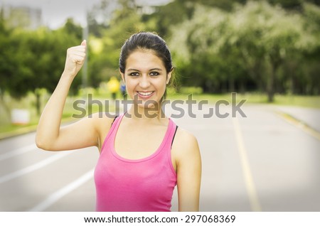 Hispanic brunette in training clothes upper body caption with confident facial expression while holding one arm up.