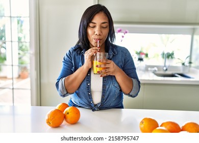 Hispanic Brunette Woman Drinking A Glass Of Fresh Orange Juice At The Kitchen