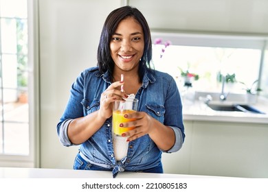 Hispanic Brunette Woman Drinking A Glass Of Fresh Orange Juice At The Kitchen