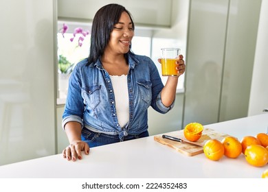 Hispanic Brunette Woman Drinking A Glass Of Fresh Orange Juice At The Kitchen