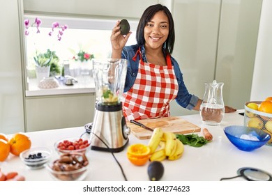 Hispanic Brunette Woman Preparing Fruit Smoothie Holding Avocado At The Kitchen