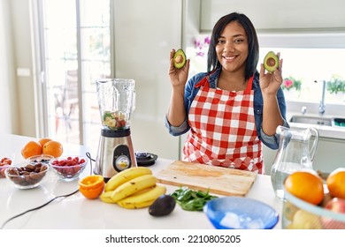 Hispanic Brunette Woman Preparing Fruit Smoothie Holding Avocado At The Kitchen