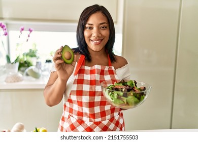 Hispanic Brunette Woman Preparing Green Salad Holding Avocado At The Kitchen