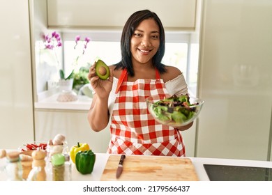 Hispanic Brunette Woman Preparing Green Salad Holding Avocado At The Kitchen