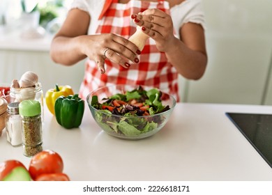 Hispanic brunette woman seasoning green salad at the kitchen - Powered by Shutterstock