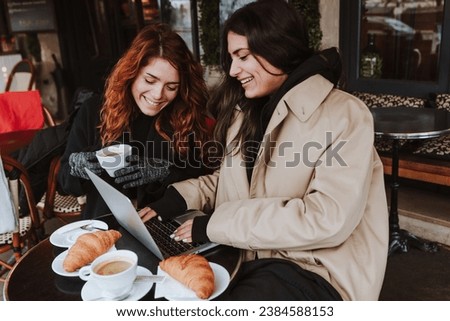 hispanic business couple of women working and using laptop at coffee shop in winter in an urban city in Europe