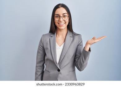 Hispanic business woman wearing glasses smiling cheerful presenting and pointing with palm of hand looking at the camera.  - Powered by Shutterstock