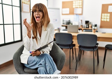 Hispanic business woman working at the office crazy and mad shouting and yelling with aggressive expression and arms raised. frustration concept. 