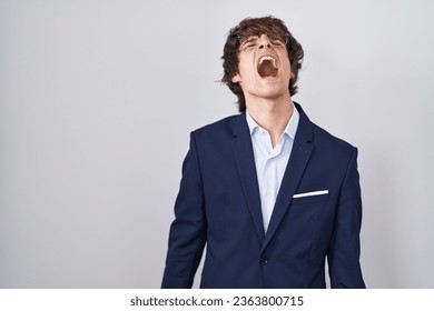 Hispanic business young man wearing glasses angry and mad screaming frustrated and furious, shouting with anger. rage and aggressive concept.  - Shutterstock ID 2363800715