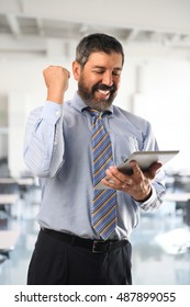 Hispanic businessman celebrating while looking at electronic tablet inside office building