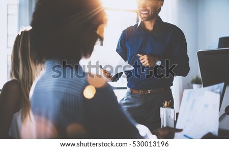 Hispanic businessman holding papers hands and smiling.Young team of coworkers making great business discussion in modern coworking office.Teamwork people concept.Horizontal, blurred background, flares