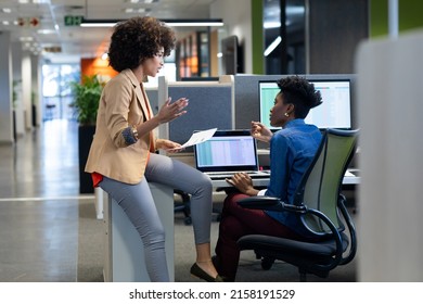 Hispanic Businesswoman Explanining Strategy To African American Female Colleague Sitting In Cubicle. Unaltered, Business, Teamwork And Modern Office Concept.