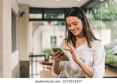 Hispanic businesswoman in formal attire in her office happy and cheerful while using smartphones and working. Young businesswoman using apps on cell phones, reading news, fast connection