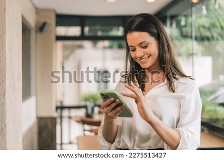 Hispanic businesswoman in formal attire in her office happy and cheerful while using smartphones and working. Young businesswoman using apps on cell phones, reading news, fast connection