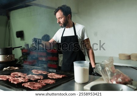 Hispanic chef adding salt to meat on a grill in a professional kitchen, getting ready to make beef tacos