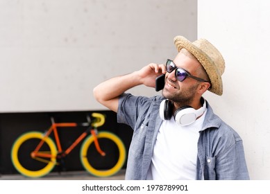 Hispanic confident man wearing a straw hat talking on the phone in front of a fixie bicycle.