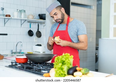 Hispanic Cook With Red Apron Preparing Food At Kitchen Of Restaurant