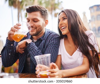 hispanic couple drinking beer on date together at outdoor patio