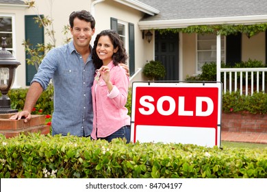 Hispanic Couple Outside Home With Sold Sign