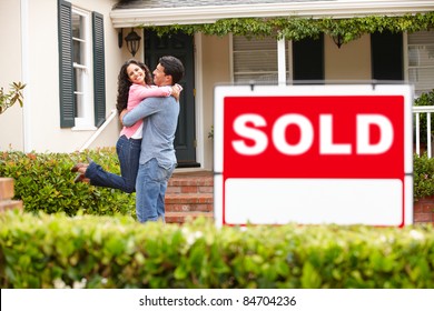 Hispanic couple outside home with sold sign