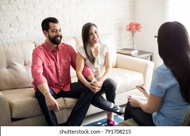 Hispanic couple sitting close to each other and holding hands while looking at their therapist