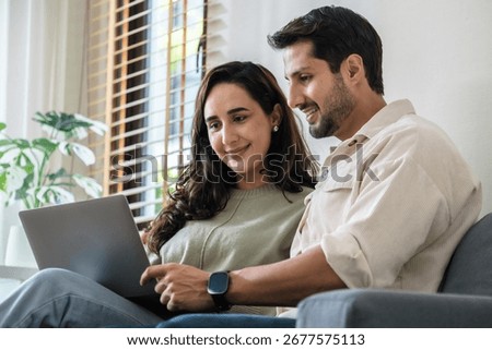 Hispanic couple using computer watching social media and streaming show together at home on the sofa 