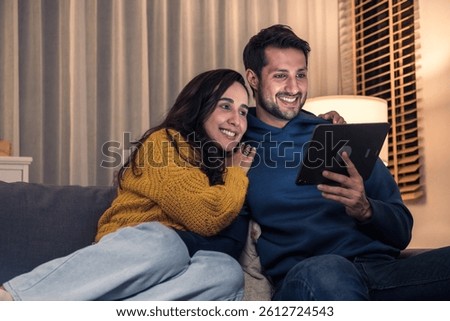 Hispanic couple using digital tablet to stream a show together at home on the sofa at night
