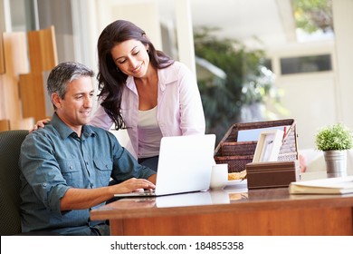 Hispanic Couple Using Laptop On Desk At Home