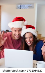 Hispanic Couple Wearing Santa Hats With Laptop Having Video Chat With Family At Christmas