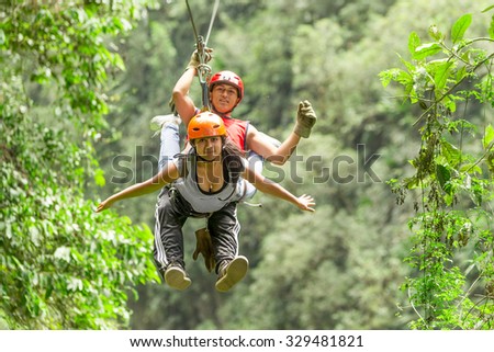 A Hispanic couple zip lining through the rainforest in Ecuador, surrounded by lush greenery and the sound of wildlife.