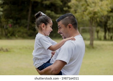 Hispanic dad hugging his little daughter in the park-father and daughter outdoors smiling face to face - Shutterstock ID 1987164311
