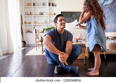 Hispanic Dad Sitting On The Floor In Sitting Room Listening His Young Daughter, Side View