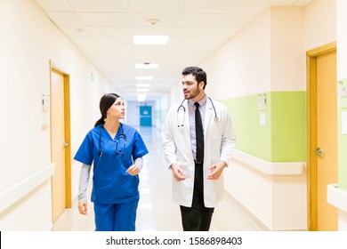 Hispanic Doctor And Nurse Talking While Walking Together In Corridor At Hospital