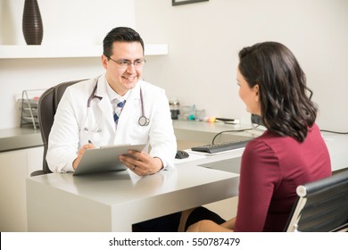 Hispanic doctor taking some notes and talking to a patient during a consultation at his office