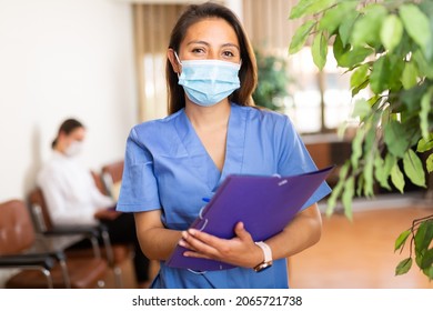 Hispanic Doctor Woman In Face Mask Standing In Medical Office With Clipboard