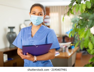 Hispanic Doctor Woman In Face Mask Standing In Medical Office With Clipboard