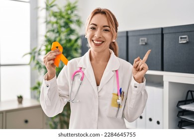 Hispanic doctor woman holding awareness orange ribbon smiling happy pointing with hand and finger to the side  - Powered by Shutterstock