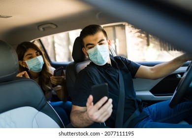 Hispanic Driver And Passenger With Face Masks Looking At The GPS Directions On The Phone App While On A Ride Share Car