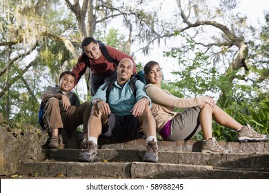 Hispanic Family With Backpacks Hiking In Park Resting