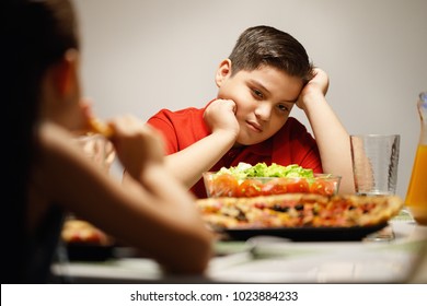 Hispanic Family With Mom, Fat Son And Daughter Having Dinner At Home, Eating Salad And Pizza. Latino People With Mother, Overweight Boy And Girl During Meal.
