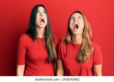 Hispanic Family Of Mother And Daughter Wearing Casual Clothes Over Red Background Angry And Mad Screaming Frustrated And Furious, Shouting With Anger. Rage And Aggressive Concept. 