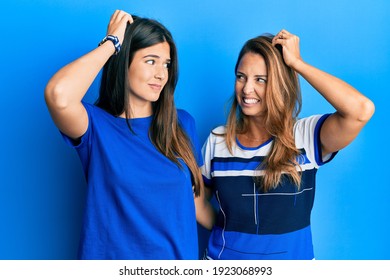 Hispanic Family Of Mother And Daughter Wearing Casual Clothes Over Blue Background Confuse And Wondering About Question. Uncertain With Doubt, Thinking With Hand On Head. Pensive Concept. 