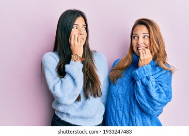 Hispanic Family Of Mother And Daughter Wearing Wool Winter Sweater Looking Stressed And Nervous With Hands On Mouth Biting Nails. Anxiety Problem. 