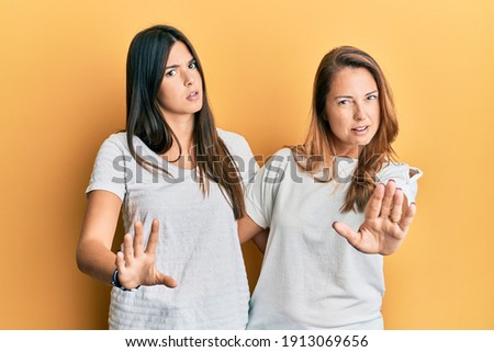 Hispanic family of mother and daughter wearing casual white tshirt doing stop gesture with hands palms, angry and frustration expression 