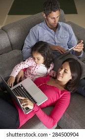 Hispanic Family On Sofa Using Laptop And Digital Tablet