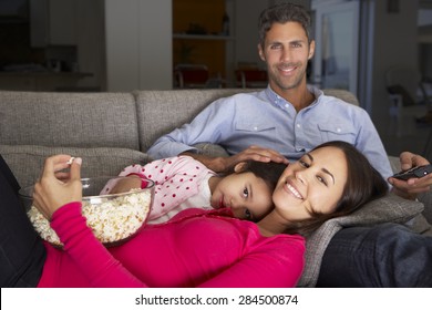 Hispanic Family On Sofa Watching TV And Eating Popcorn