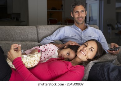 Hispanic Family On Sofa Watching TV And Eating Popcorn