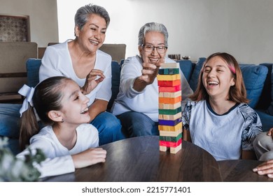 Hispanic Family Playing Jenga Game With Grandmother And Daughter At Home, Three Generations Of Women In Mexico Latin America