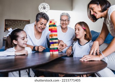 Hispanic Family Playing Jenga Game With Grandmother And Daughter At Home, Three Generations Of Women In Mexico Latin America