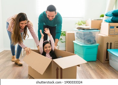 Hispanic Family Playing In The Living Room While Packing Their Furniture And Things. Young Woman And Man Pushing A Little Girl Inside A Cardboard Box